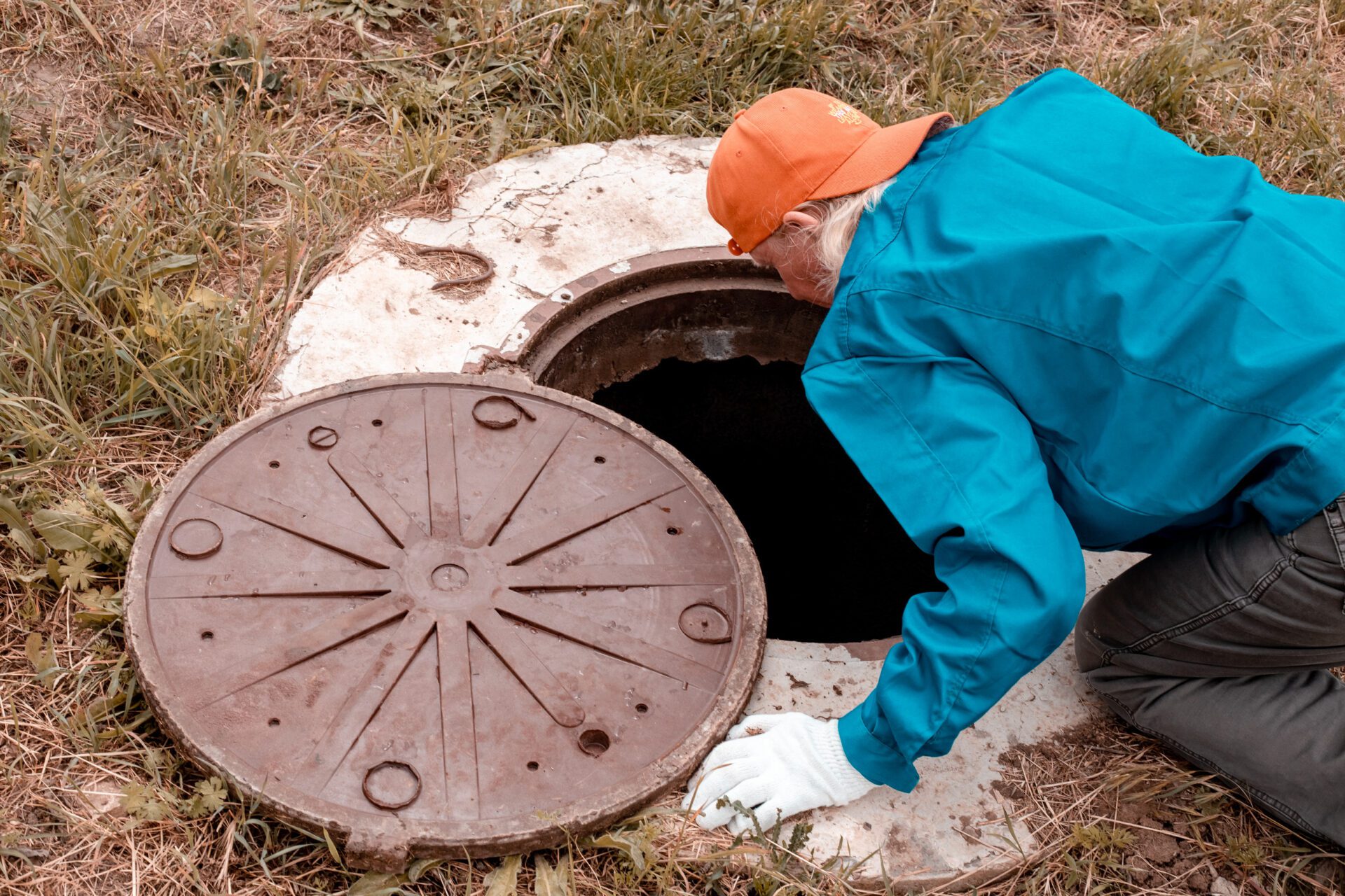 Worker inspecting open septic tank during maintenance or cleaning in an outdoor grassy area.